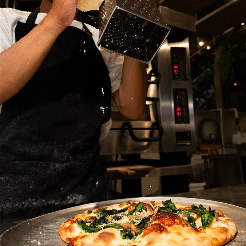 Chef grating fresh cheese on pizza at Doughboys Bali